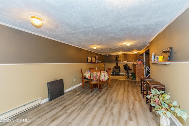 dining space featuring crown molding, a textured ceiling, a wood stove, light hardwood / wood-style floors, and a baseboard heating unit