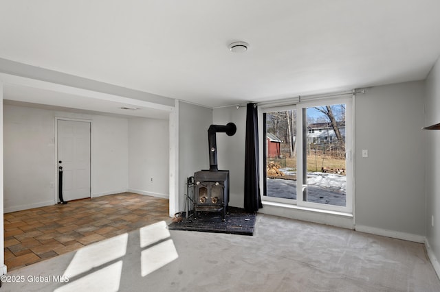 unfurnished living room with stone finish flooring, baseboards, and a wood stove