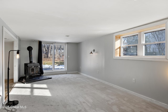 unfurnished living room featuring baseboards, carpet, and a wood stove