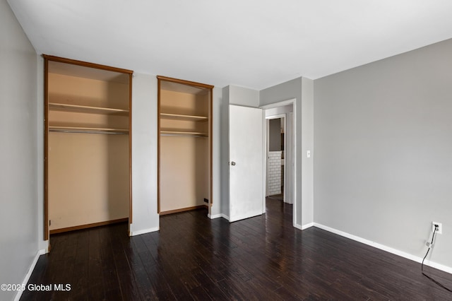 unfurnished bedroom featuring baseboards, multiple closets, and hardwood / wood-style floors