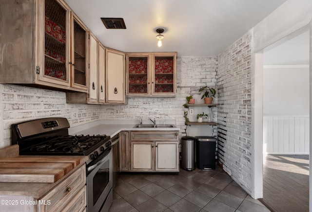 kitchen featuring visible vents, glass insert cabinets, light countertops, stainless steel gas stove, and dark tile patterned flooring