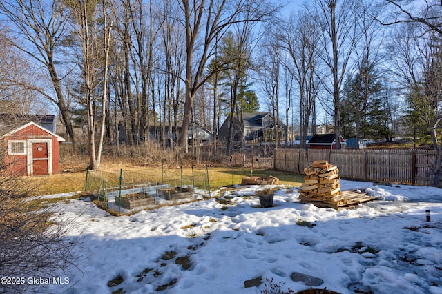 snowy yard featuring a garden, a storage unit, an outdoor structure, and fence