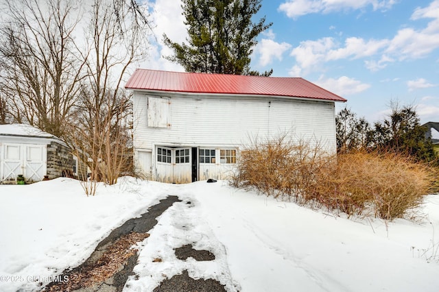 snow covered property with a garage, metal roof, and an outdoor structure