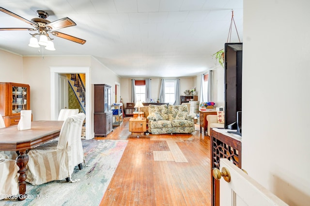 living room with a ceiling fan, light wood-style flooring, stairway, and crown molding