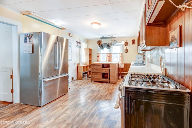 kitchen with light wood finished floors, gas range oven, light countertops, freestanding refrigerator, and a sink