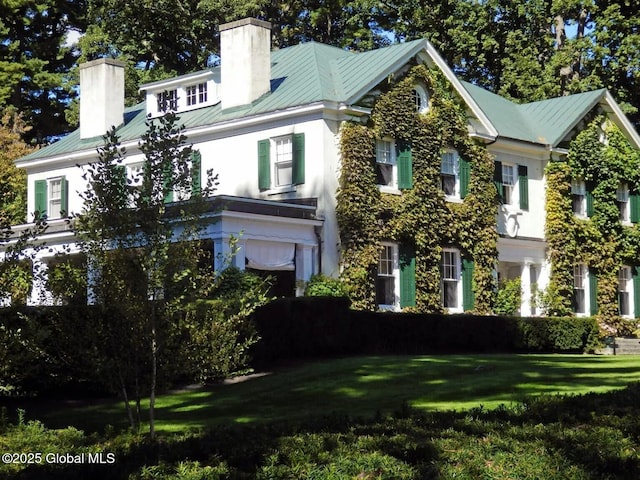 view of front of property featuring metal roof, a chimney, a front yard, and stucco siding