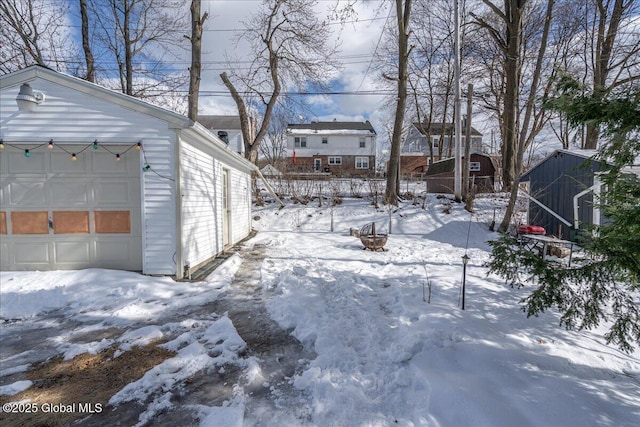 snowy yard with a detached garage and an outbuilding