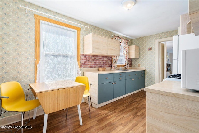 kitchen featuring light brown cabinets, a sink, wood finished floors, light countertops, and wallpapered walls