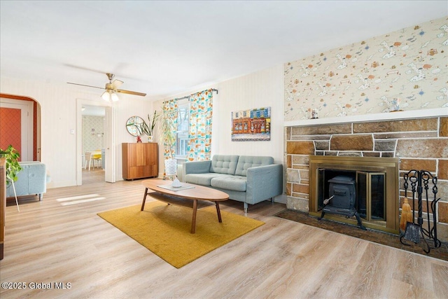 living room with ceiling fan, wallpapered walls, a fireplace, and wood finished floors