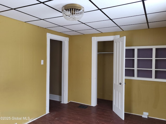 unfurnished bedroom with dark hardwood / wood-style flooring, a paneled ceiling, a closet, and an inviting chandelier