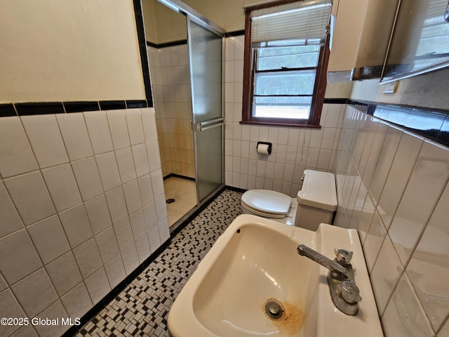 bathroom with toilet, sink, a shower with door, and tile walls