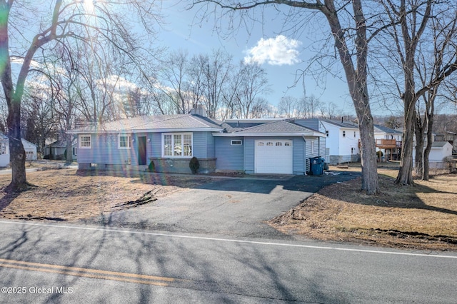 ranch-style home featuring aphalt driveway, a residential view, roof with shingles, an attached garage, and a chimney