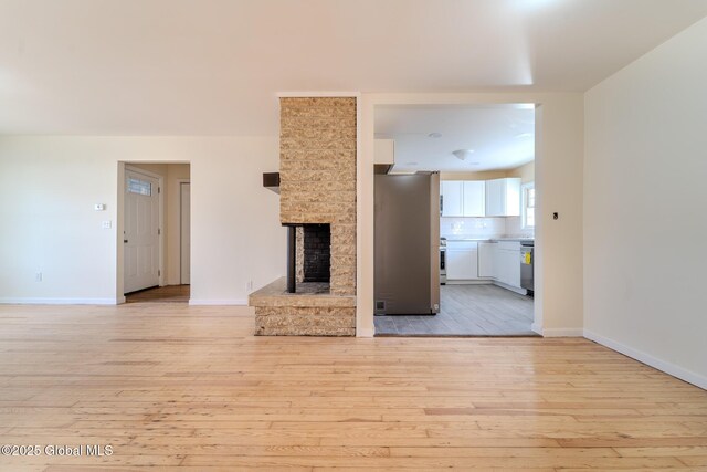 unfurnished living room featuring a multi sided fireplace, light wood-style flooring, and baseboards