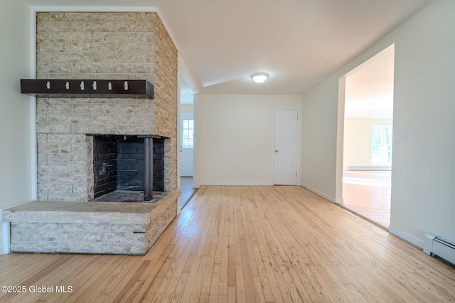 unfurnished living room with hardwood / wood-style floors, a brick fireplace, baseboards, and a baseboard radiator