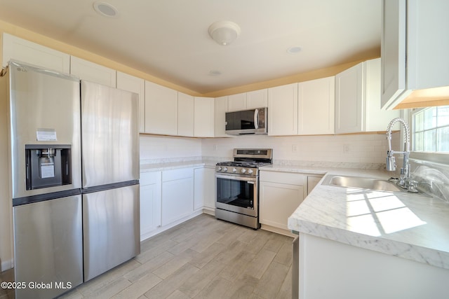 kitchen with a sink, white cabinets, backsplash, and stainless steel appliances