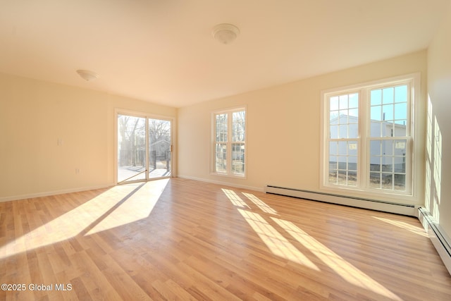 spare room featuring a baseboard radiator, baseboards, and light wood finished floors