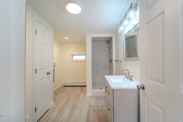 bathroom with vanity, wood finished floors, baseboards, tiled shower, and baseboard heating