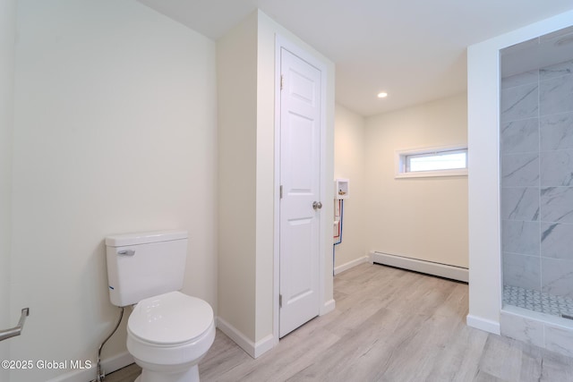 bathroom with toilet, wood finished floors, baseboard heating, and tiled shower