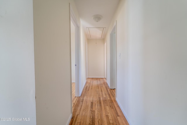 corridor featuring light wood-style flooring, attic access, and baseboards