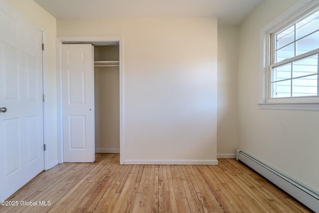 unfurnished bedroom featuring baseboards, light wood-type flooring, a closet, and a baseboard radiator