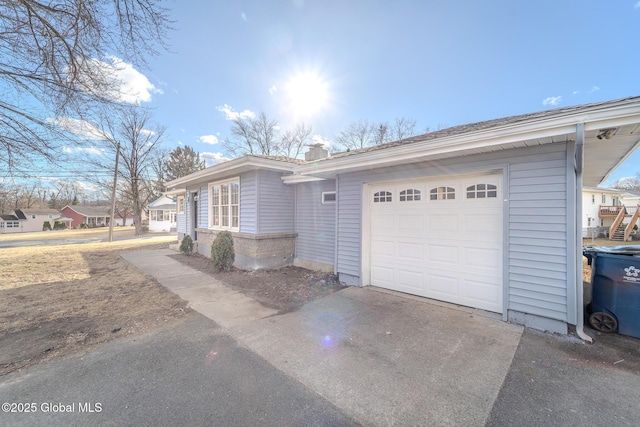 view of side of property with an attached garage, a chimney, and driveway