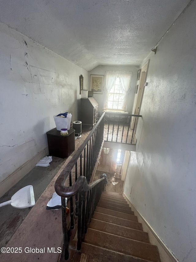 stairway featuring wood-type flooring, lofted ceiling, and a textured ceiling