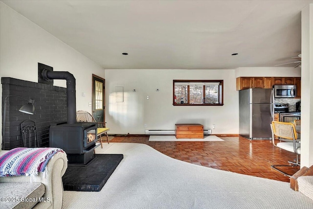 living area with a baseboard heating unit, a wealth of natural light, and a wood stove