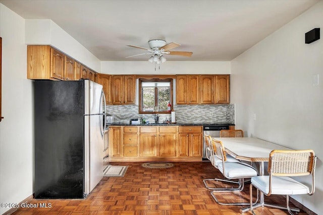 kitchen featuring ceiling fan, appliances with stainless steel finishes, brown cabinets, tasteful backsplash, and dark countertops