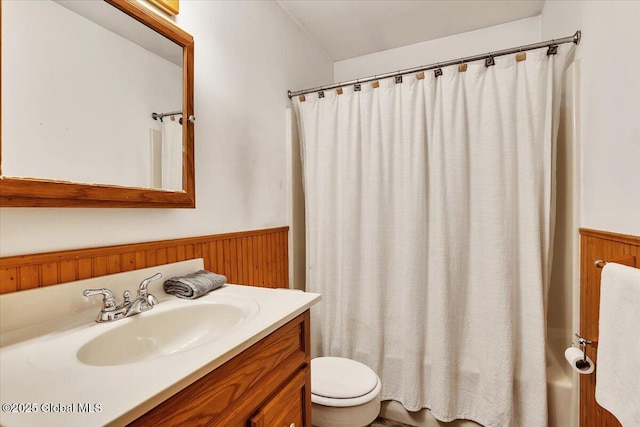 bathroom with toilet, wood walls, vanity, and wainscoting