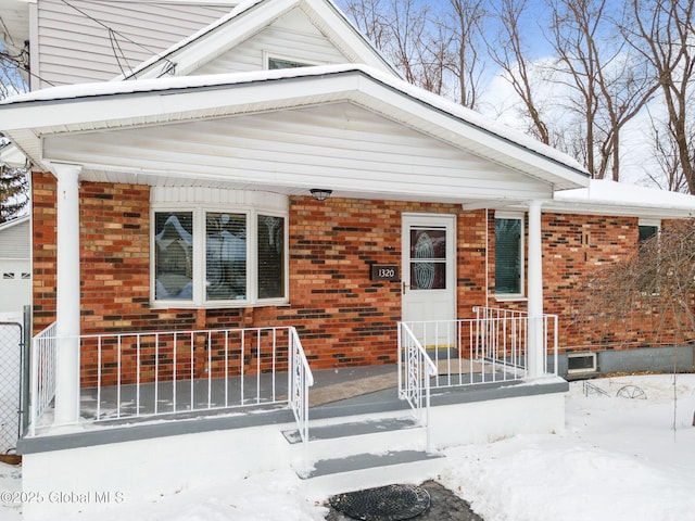 snow covered property entrance with brick siding and a porch