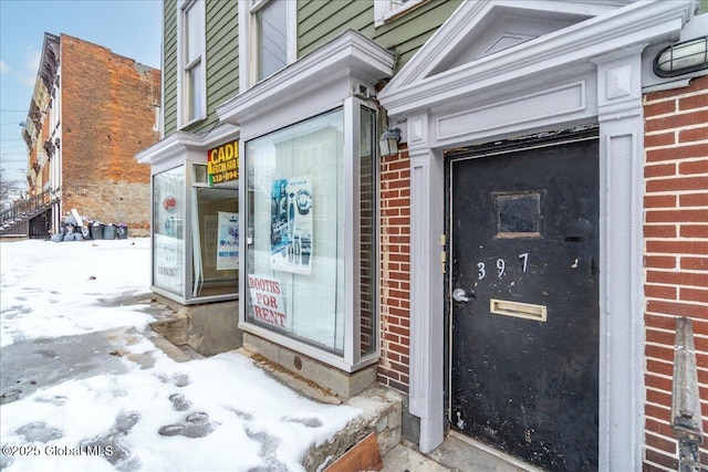 snow covered property entrance featuring brick siding