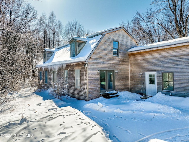 snow covered back of property with entry steps and a gambrel roof