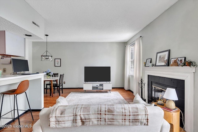 living room with a tile fireplace, light hardwood / wood-style flooring, an inviting chandelier, and a textured ceiling