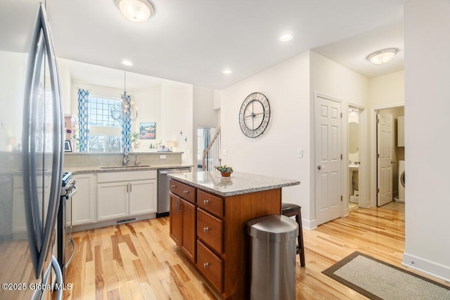 kitchen featuring white cabinetry, hanging light fixtures, appliances with stainless steel finishes, light wood-type flooring, and a center island