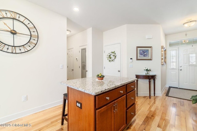 kitchen with baseboards, a breakfast bar, a center island, light stone countertops, and light wood-type flooring