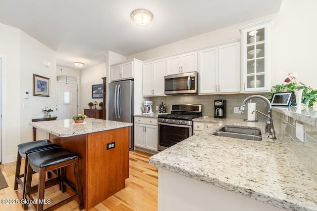 kitchen featuring stainless steel appliances, a sink, white cabinetry, a center island, and glass insert cabinets