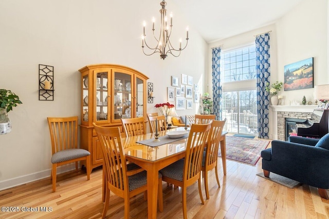 dining space featuring baseboards, a towering ceiling, an inviting chandelier, light wood-type flooring, and a fireplace