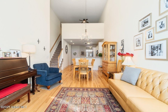 living room featuring a towering ceiling, an inviting chandelier, stairway, and wood finished floors