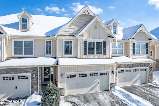 view of front of home with an attached garage, stone siding, driveway, and board and batten siding