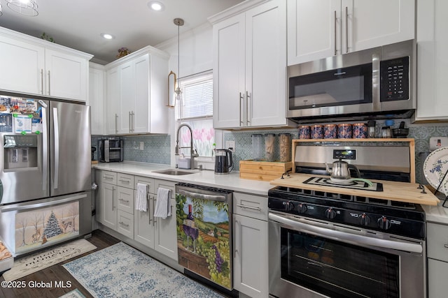 kitchen with hanging light fixtures, stainless steel appliances, light countertops, white cabinetry, and a sink