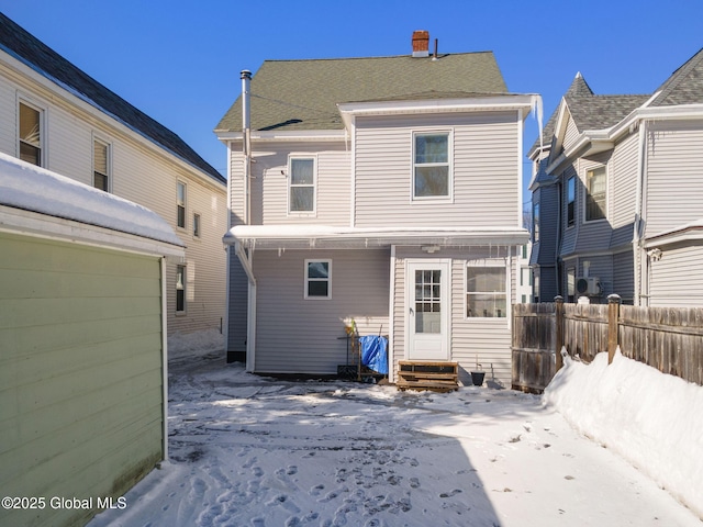 snow covered rear of property featuring entry steps and fence