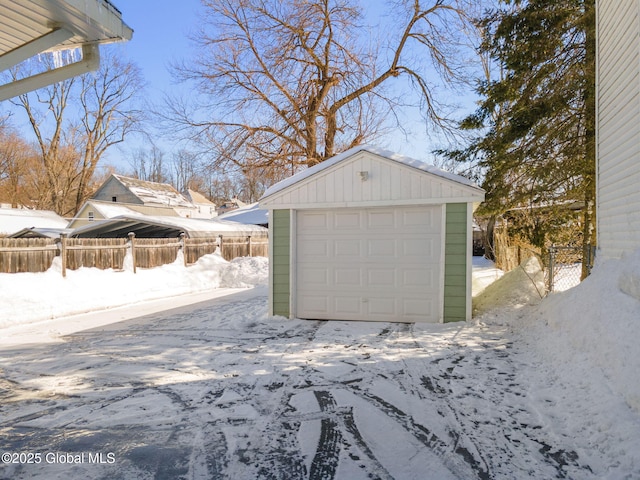 snow covered garage featuring a detached garage and fence