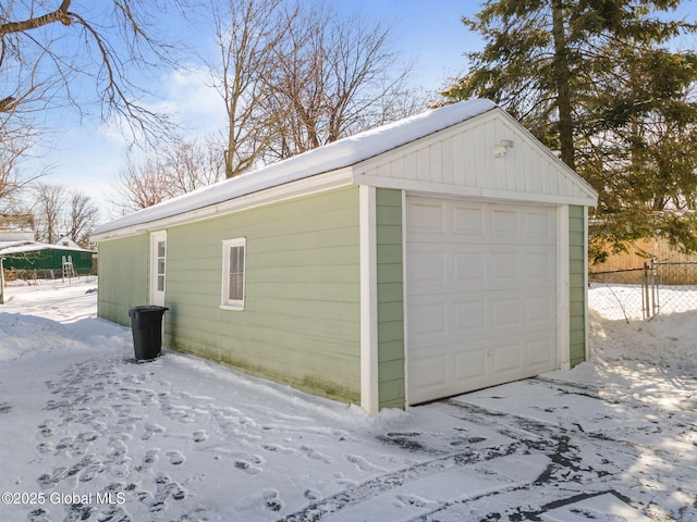 snow covered garage featuring a garage and fence