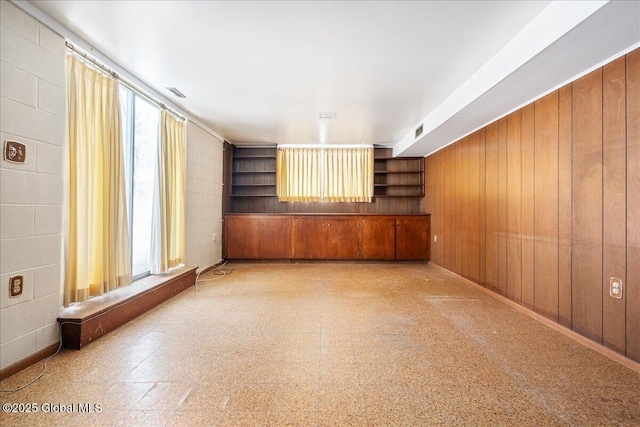 unfurnished living room with visible vents, a healthy amount of sunlight, and concrete block wall