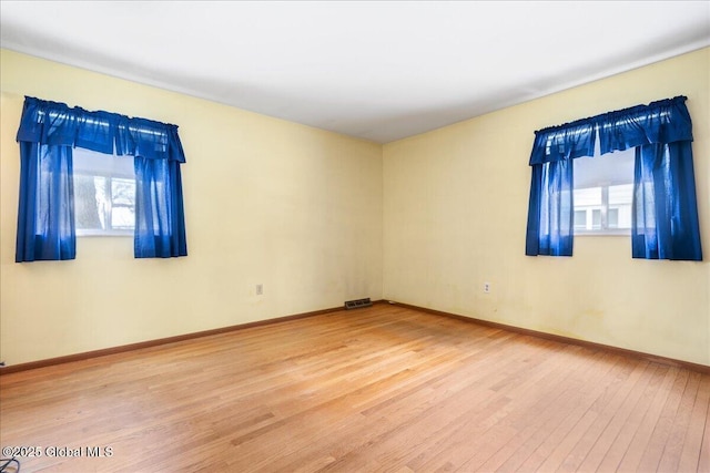 empty room with visible vents, light wood-style flooring, and baseboards