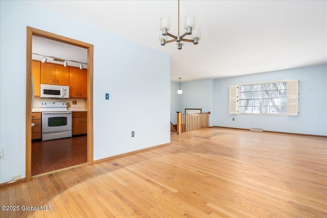 unfurnished living room with rail lighting, light wood-style floors, baseboards, and a chandelier