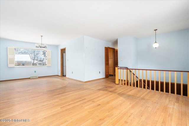 spare room with an inviting chandelier, light wood-style floors, baseboards, and visible vents