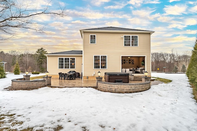 snow covered back of property with a garage, a patio area, a hot tub, and an outdoor hangout area