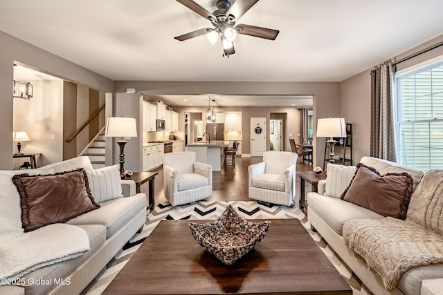 living room with stairs, ceiling fan with notable chandelier, and light wood-style floors