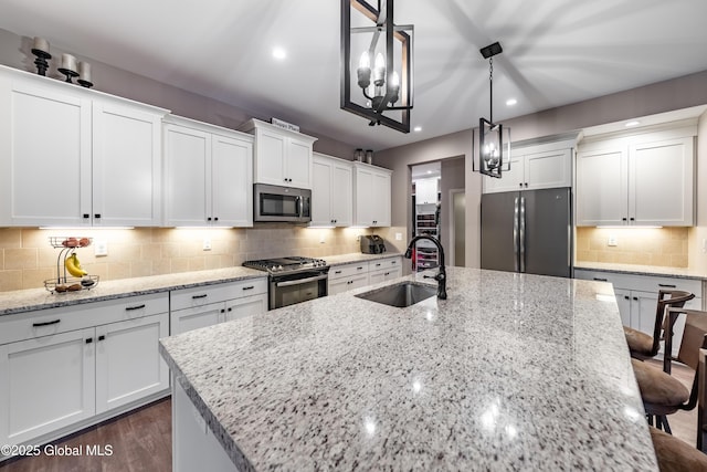 kitchen featuring stainless steel appliances, a sink, white cabinetry, backsplash, and an island with sink